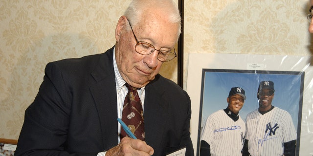 El miembro del Salón de la Fama Bob Feller firma una pelota de béisbol