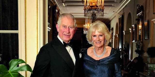 King Charles in a tuxedo next to Camilla in a navy blue gown with jewels