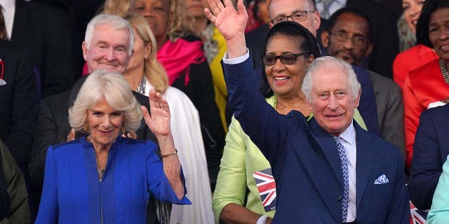 Britain's King Charles III (R) and Britain's Queen Camilla wave as they arrive to attend the Coronation Concert at Windsor Castle