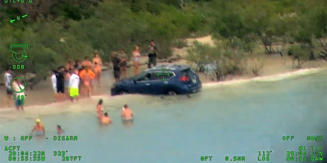 SUV in the water while a crowd stands around.