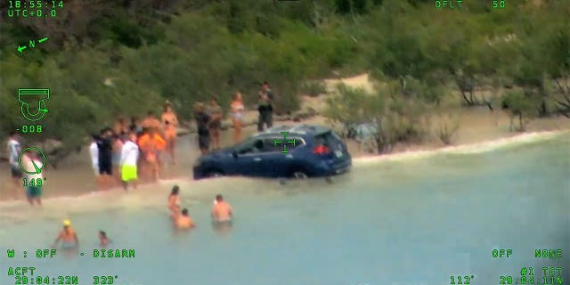 SUV in the water while a crowd stands around.