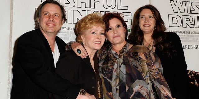 Todd Fisher in a black suit holds on to his mother Debbie Reynolds, also in black, who hugs her daughter Carrie Fisher in a multi-patterned blouse next to sister Joely in a black jacket on the red carpet