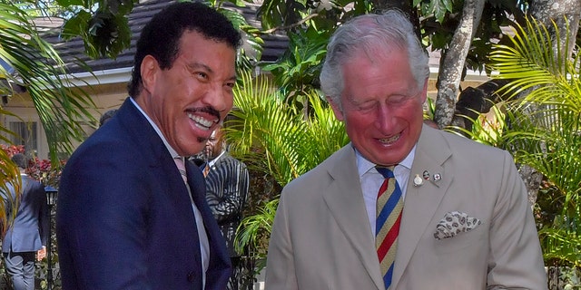 Lionel Richie in a blue jacket laughs with the then Prince Charles in a light tan suit and striped tie while together in Barbados