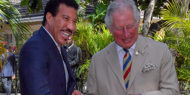 Lionel Richie in a blue jacket laughs with the then Prince Charles in a light tan suit and striped tie while together in Barbados