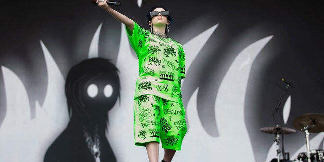 Billie Eilish holds her microphone out to the audience in a green matching shorts and t-shirt set in Middlesbrough, England