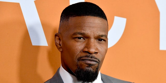 Jamie Foxx gives a cool pout on the carpet, wearing a white button down and grey suit