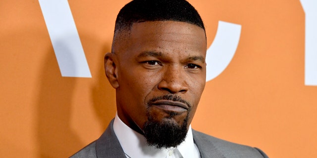 Jamie Foxx gives a cool pout on the carpet, wearing a white button down and grey suit