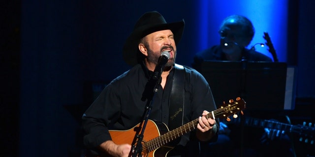 Garth Brooks performs on stage in all black with a guitar