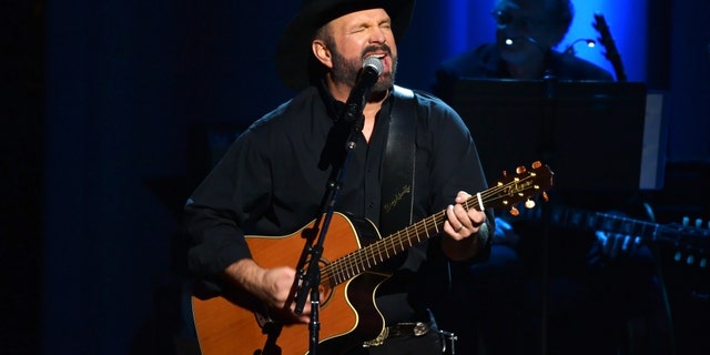 Garth Brooks performs on stage with a guitar in all black outfit