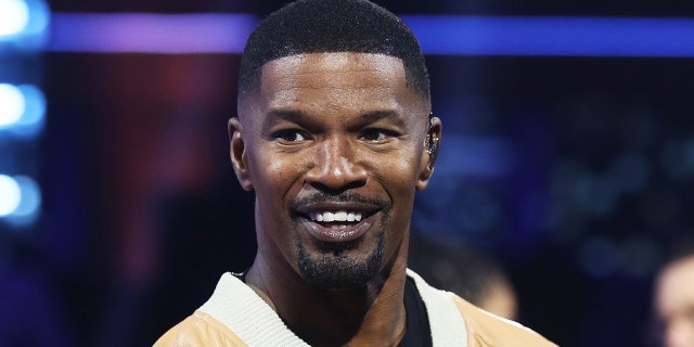 Jamie Foxx in a yellow jacket with white trim smiles on the set of "BEAT SHAZAM"