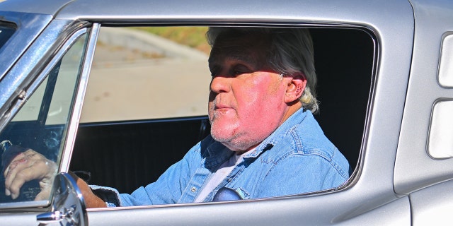 Jay Leno wearing denim driving his car shows off his relatively fresh burn on his cheek while driving in Los Angeles