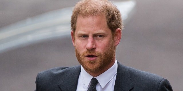 Prince Harry in a dark grey suit and tie looks off to his left while walking into High Court