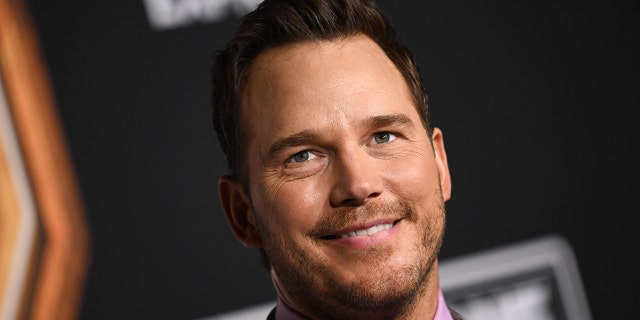 Chris Pratt smiles and looks upward in a bright lilac shirt and suit on the red carpet