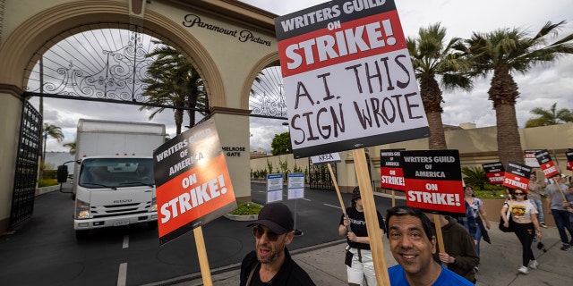 Writers on strike in Los Angeles carry signs that highlight what they take issue with, with one sign saying "A.I. THIS SIGN WROTE"