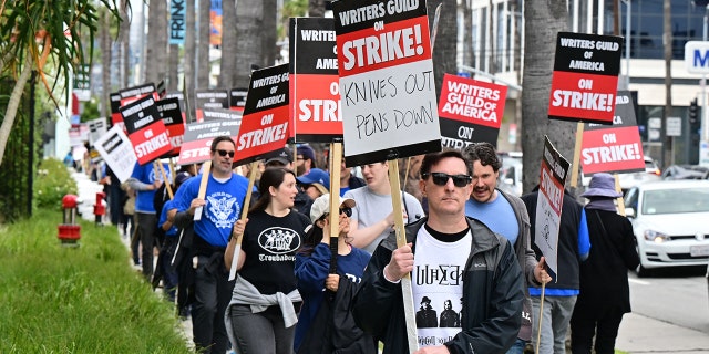 Writer Eric Heisserer holds his writers strike sign on the fourth day of the writers strike in front of Netflix in Hollywood, followed by many other individuals