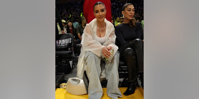 Kim Kardashian wears a tank top, transparent poncho, flare jeans and denim shoes courtside at the Lakers