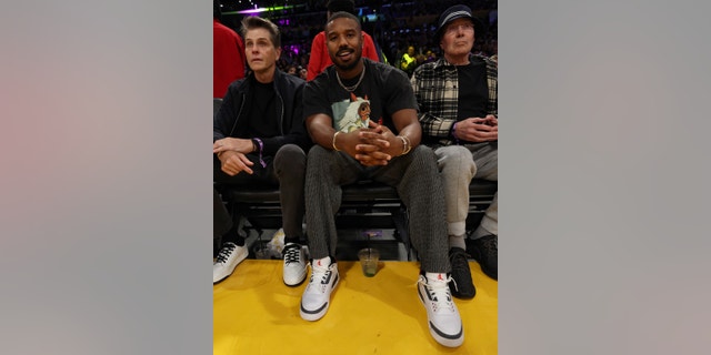 Michael B. Jordan smiles for a photo courtside, wearing a black Princess Mononoke shirt at the Laker's game