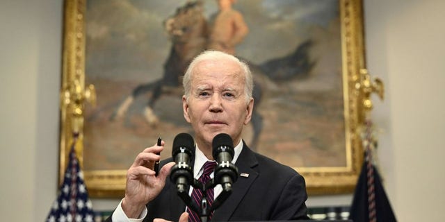 Biden speaks on a microphone in front of a painting