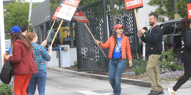 Justine Bateman in a red hat, blue shirt, and red jacket protests in Hollywood during the Writer's Strike