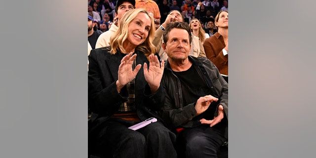 Michael J. Fox looks up courtside at the Knick game in New York, sitting next to his wife Tracy who has her hands upwards