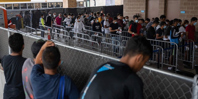 Migrants standing at a fence for a bus