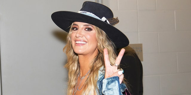 Lainey Wilson gives the cameras a peace sign as she walks inside the Country Music Awards, wearing a black brimmed hat