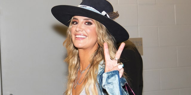 Lainey Wilson gives the cameras a peace sign as she walks inside the Country Music Awards, wearing a black brimmed hat