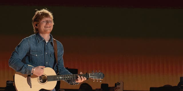 Ed Sheeran wears a denim shirt while performing with a guitar.