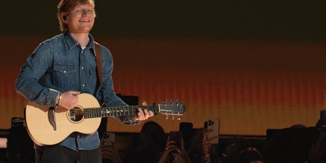 Ed Sheeran wears a denim shirt while performing with a guitar.