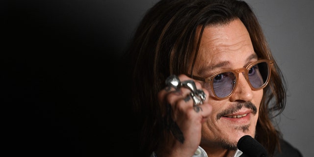 Johnny Depp kannab pruuni äärega siniste klaasidega prille ja räägib Cannes'is pressi ajal mikrofoni