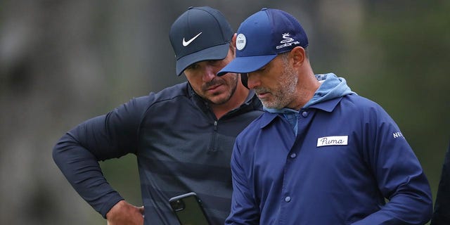 Brooks Koepka y el entrenador Claude Harmon III hablan durante una ronda de práctica en el Campeonato PGA 2020