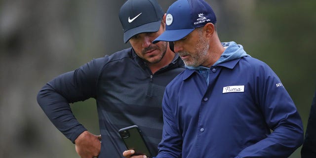 Brooks Koepka y el entrenador Claude Harmon III hablan durante una ronda de práctica en el Campeonato PGA 2020