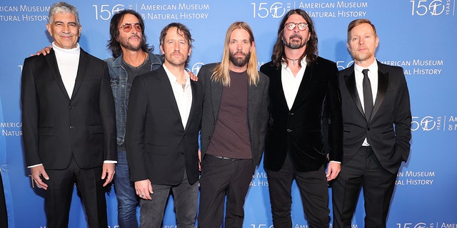 The Foo Fighters stand next to each other in front of a blue backdrop at the American Museum of Natural History Gala