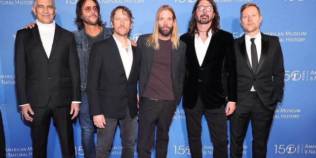 The Foo Fighters stand next to each other in front of a blue backdrop at the American Museum of Natural History Gala