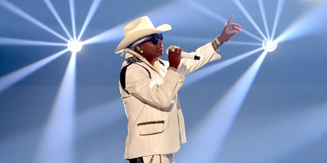 Jimmie Allen performs onstage in a white suit and cowboy hat