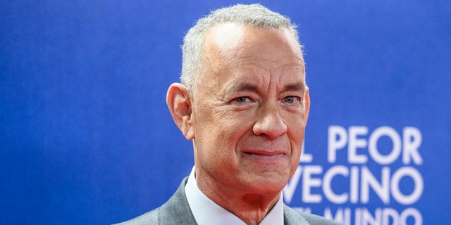 Tom Hanks soft smiles on the red carpet with short grey hair in a grey suit while in Madrid