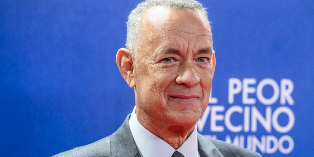 Tom Hanks soft smiles on the red carpet with short grey hair in a grey suit while in Madrid