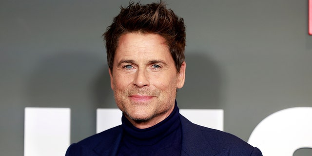 Rob Lowe soft smiles in a black turtleneck and blue suit at the premiere of his Netflix show "Unstable"