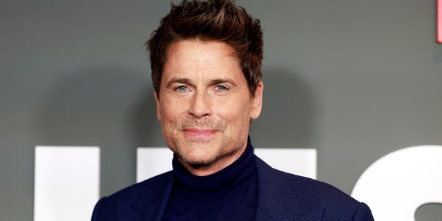 Rob Lowe soft smiles in a black turtleneck and blue suit at the premiere of his Netflix show "Unstable"