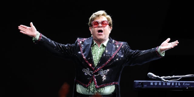 Elton John with his arms out to the crowd on stage