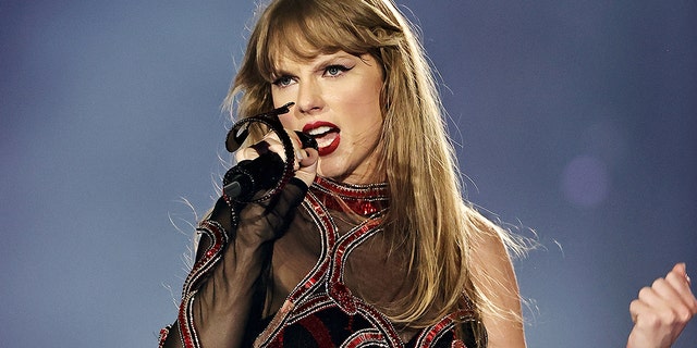 Taylor Swift in her Reputation era jumpsuit sings into a microphone while on stage at the Eras Tour