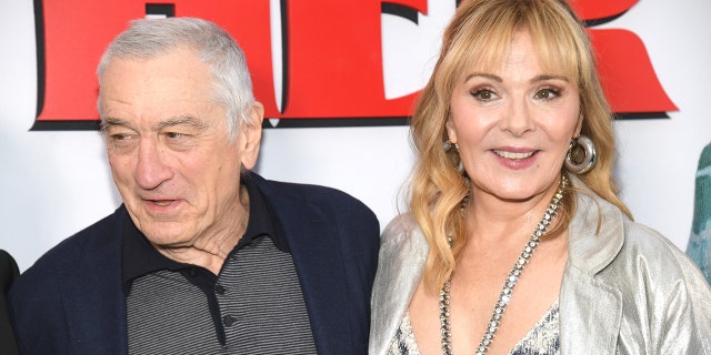 Robert De Niro looks to his right on the red carpet of his new film "About My Father" with co-star Kim Cattrall in a sparkly outfit with a deep V cut