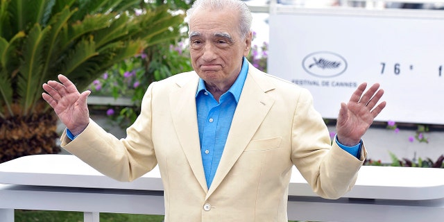 Martin Scorsese with his arms outstretched in a tan suit and bright blue button down at Cannes Film festival