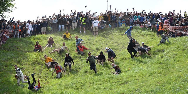 Competitors chase a wheel of cheese during the annual cheese rolling race in the UK