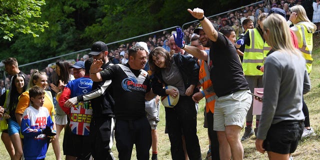 A woman is helped up after winning a cheese rolling race