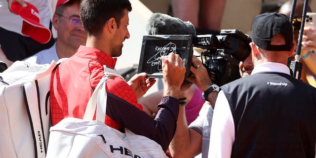 Novak Djokovic signs the camera after winning his first round match at the French Open