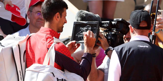 Novak Djokovic signs the camera after winning his first round match at the French Open