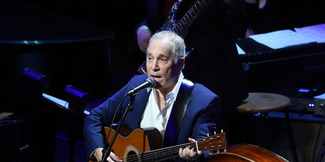 Paul Simon performing with a guitar on stage in 2015.