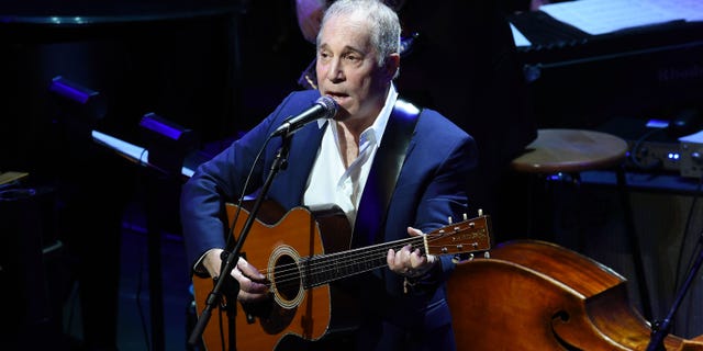 Paul Simon performing with a guitar on stage in 2015.