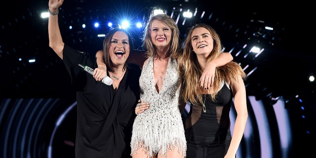 Taylor Swift in a silver sparkly outfit holds on to Mariska Hargitay and Cara Delevingne during her concert